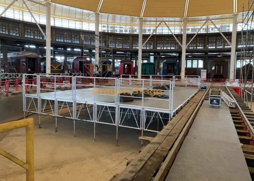  Podium de scène avec garde-corps en aluminium 12x8m avec 2 escaliers d'accès et rampe de chargement/déchargement le long de la scène arrière